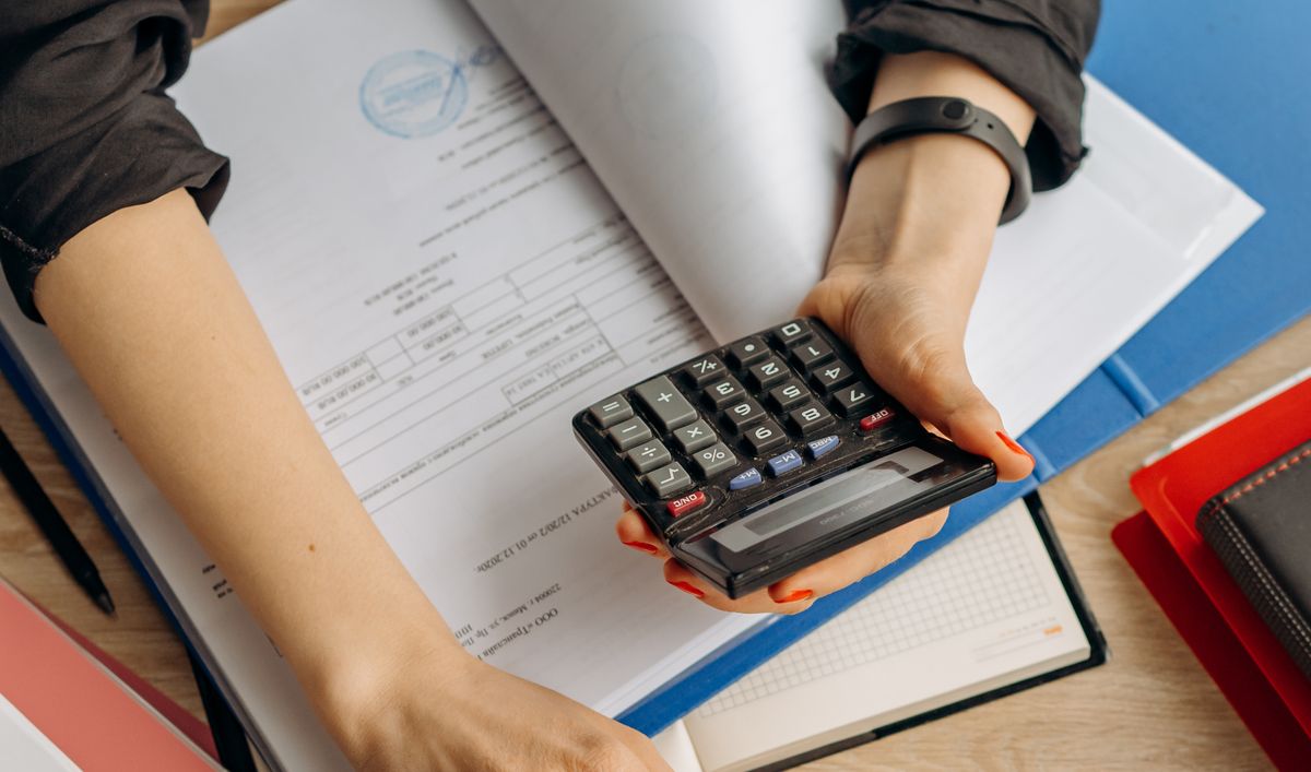 Gerente usando una calculadora sobre documentos de presupuesto para planificar el costo de capacitación en idiomas por empleado